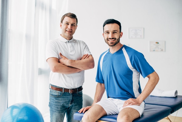 smiling Physiotherapist and football player in hospital looking at camera